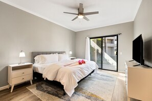 Une chambre à coucher moderne, équipée d’un lit, de tables de chevet, d’un téléviseur et d’un ventilateur de plafond.
