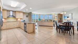 Una cocina moderna con una isla central, comedor con mesa y sillas, y vista al mar a través de amplios ventanales.