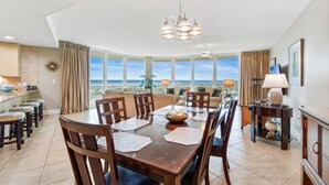 Un comedor con vistas al océano, una cocina con barra y una sala de estar con un ventanal grande.