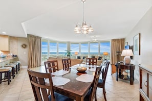 A dining area with a view of the ocean, a kitchen with a bar, and a living area with a large window.