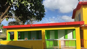 Un bâtiment aux couleurs vives, avec un toit rouge, des murs verts et jaunes, et une entrée fermée par un portail.