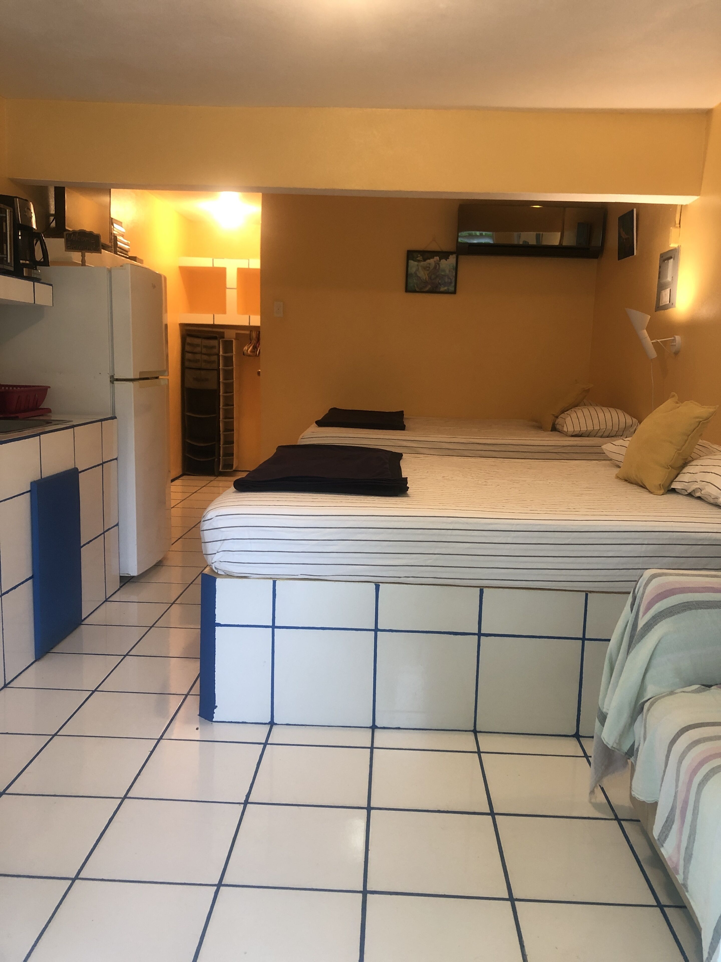 Ein kleines Zimmer mit einer Küchenzeile an einer Seite, einem Bett mit gestreifter Bettwäsche und einem kleinen Tisch.