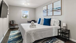 A hotel room with a bed, a desk, a chair, a TV, and artwork on the wall. - Gazebo-4BR Ping Pong-Arcade Room (Rapid City)