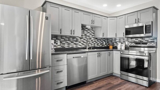 A modern kitchen with stainless steel appliances, grey cabinets, and a tiled backsplash. - Gazebo-4BR Ping Pong-Arcade Room (Rapid City)