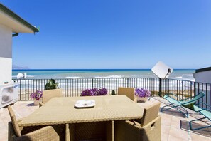 A balcony with wicker furniture, a table, and chairs facing the ocean.