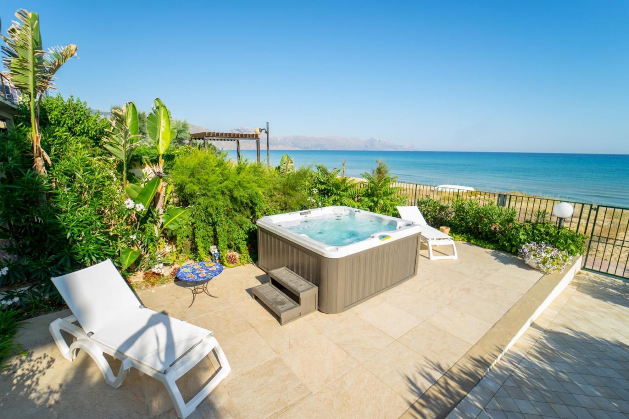 A patio with a hot tub, lounge chairs, and a view of the sea.