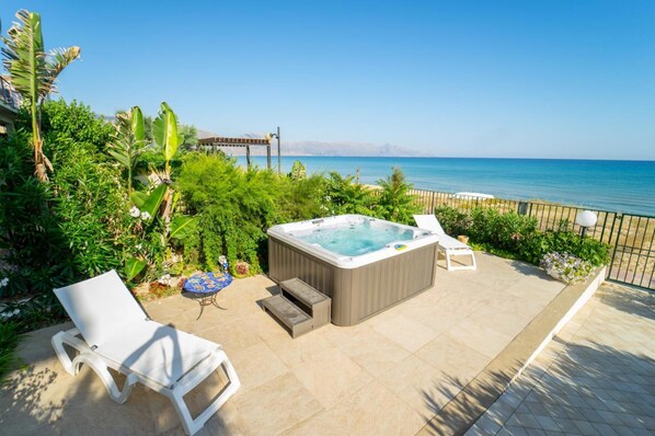 A patio with a hot tub, lounge chairs, and a view of the sea.