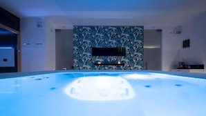 A modern spa area with a hot tub, a wall-mounted TV, and a tropical leaf-patterned wall.