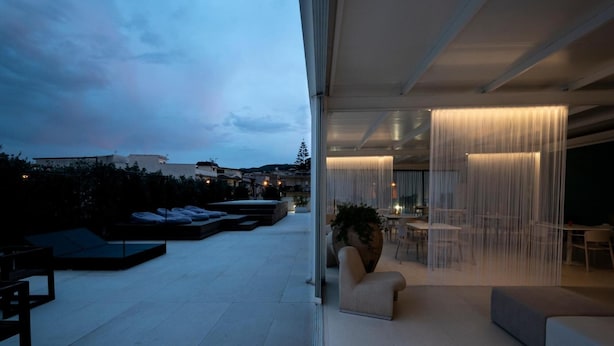 A modern rooftop terrace with a glass partition, outdoor seating, and a view of the cityscape.