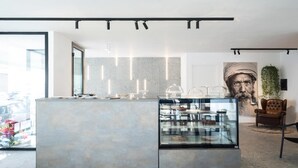 Un intérieur moderne avec un comptoir central où sont exposés des produits alimentaires, une grande fenêtre et une œuvre d’art accrochée au mur.