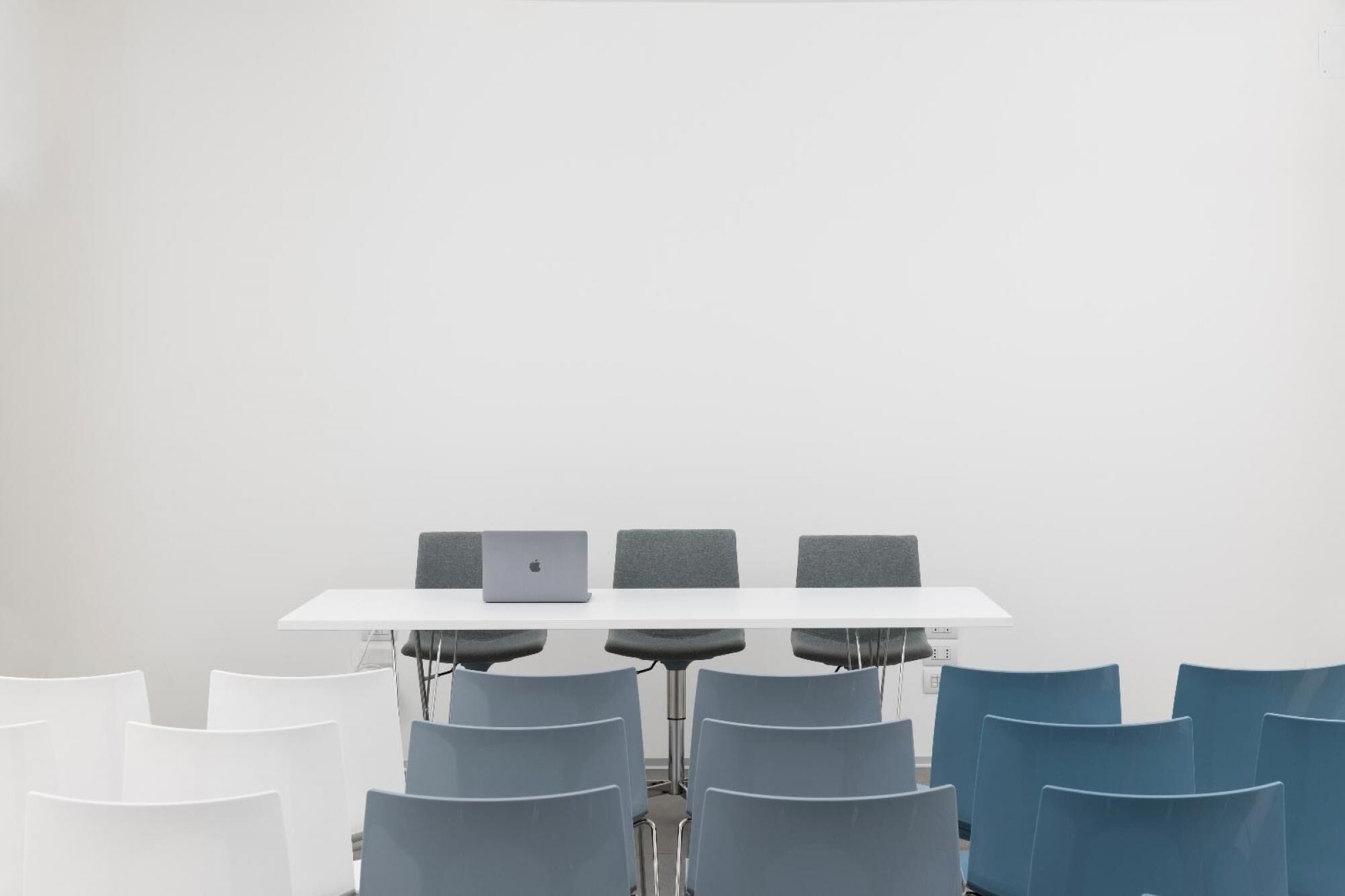 A conference room with a white table, four grey chairs, and a laptop on the table.