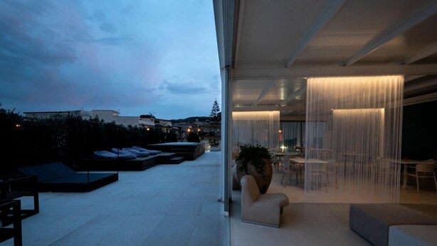 Une terrasse moderne sur le toit, dotée d’une paroi en verre, d’un espace salon extérieur et offrant une vue sur le paysage urbain.