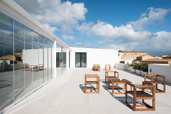 A rooftop terrace with glass walls, wooden furniture, and a clear view of the cityscape. - Alkamuri Posh Hotel Spa 103 Suite Superior (Alcamo)