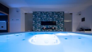 A modern spa room with a hot tub, a wall-mounted TV, and a tropical leaf-patterned wall.