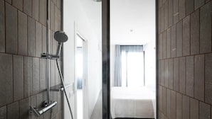A modern bathroom with a glass-enclosed shower, a visible door leading to a bedroom with a bed and curtains. - Alkamuri Posh Hotel Spa 108 Suite Superior (Alcamo)