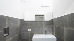 Ein modernes Badezimmer mit einem weißen Waschbecken, dunklen Fliesenwänden und einem Spiegel über dem Waschbecken.