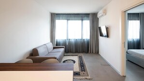 Ein modernes Hotelzimmer mit einer Couch, einem an der Wand montierten Fernseher und einem Bett.