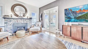 A spacious living room with a stone fireplace, comfortable seating, a large flat-screen TV, and a scenic mountain view.