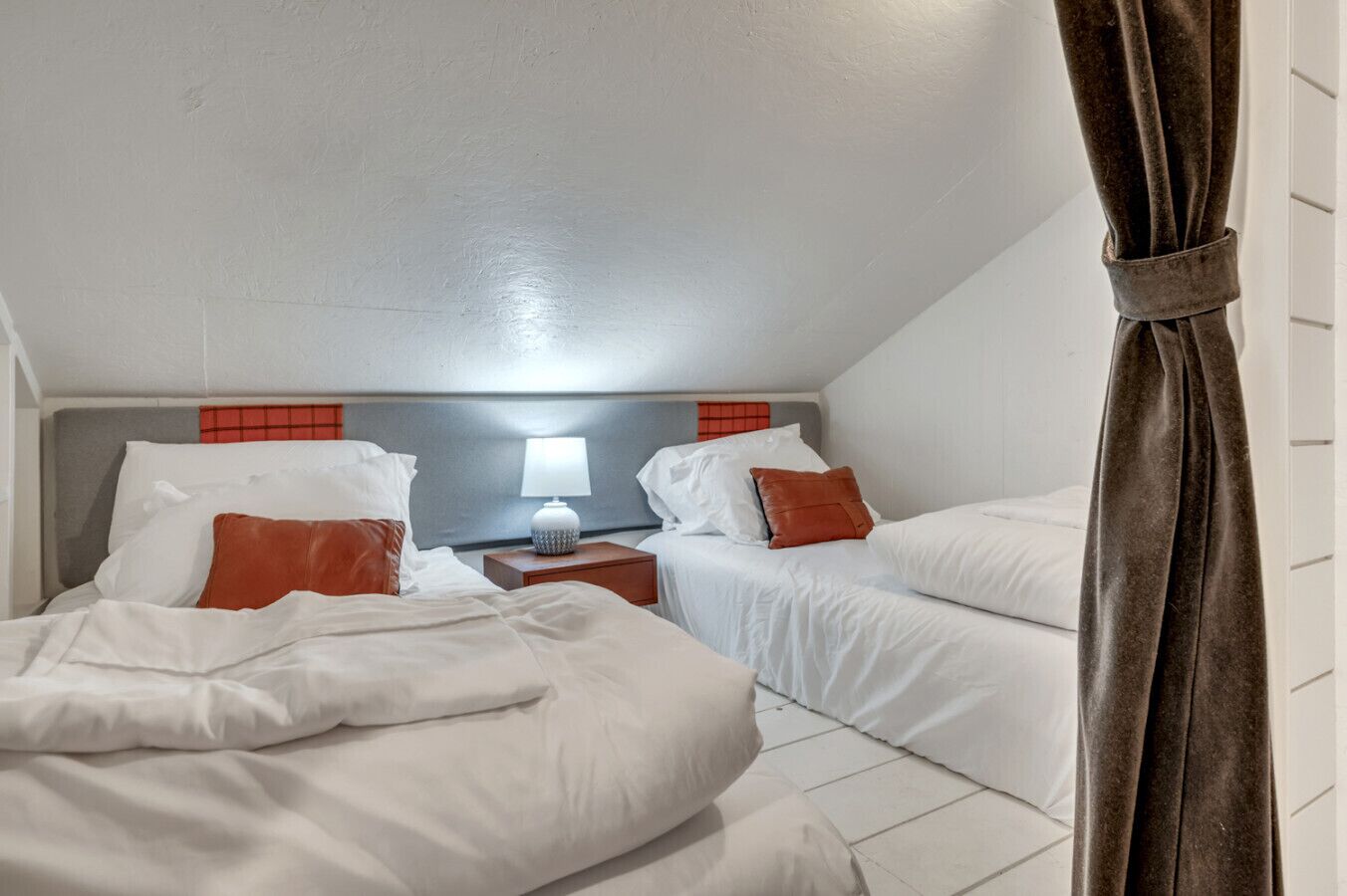 Una habitación de hotel con dos camas, una mesita de noche, una lámpara y una cortina.