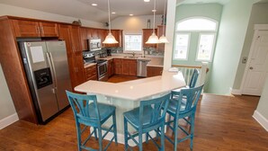 A kitchen with wooden cabinets, stainless steel appliances, a central island with bar stools, and pendant lighting. - Oceanside, Pool Table, Private Pool, Close to Beach! OS9Q, Someday Came (Corolla)