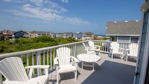A wooden deck with white Adirondack chairs and a small table, overlooking a beach with houses in the background. - Oceanside, Pool Table, Private Pool, Close to Beach! OS9Q, Someday Came (Corolla)