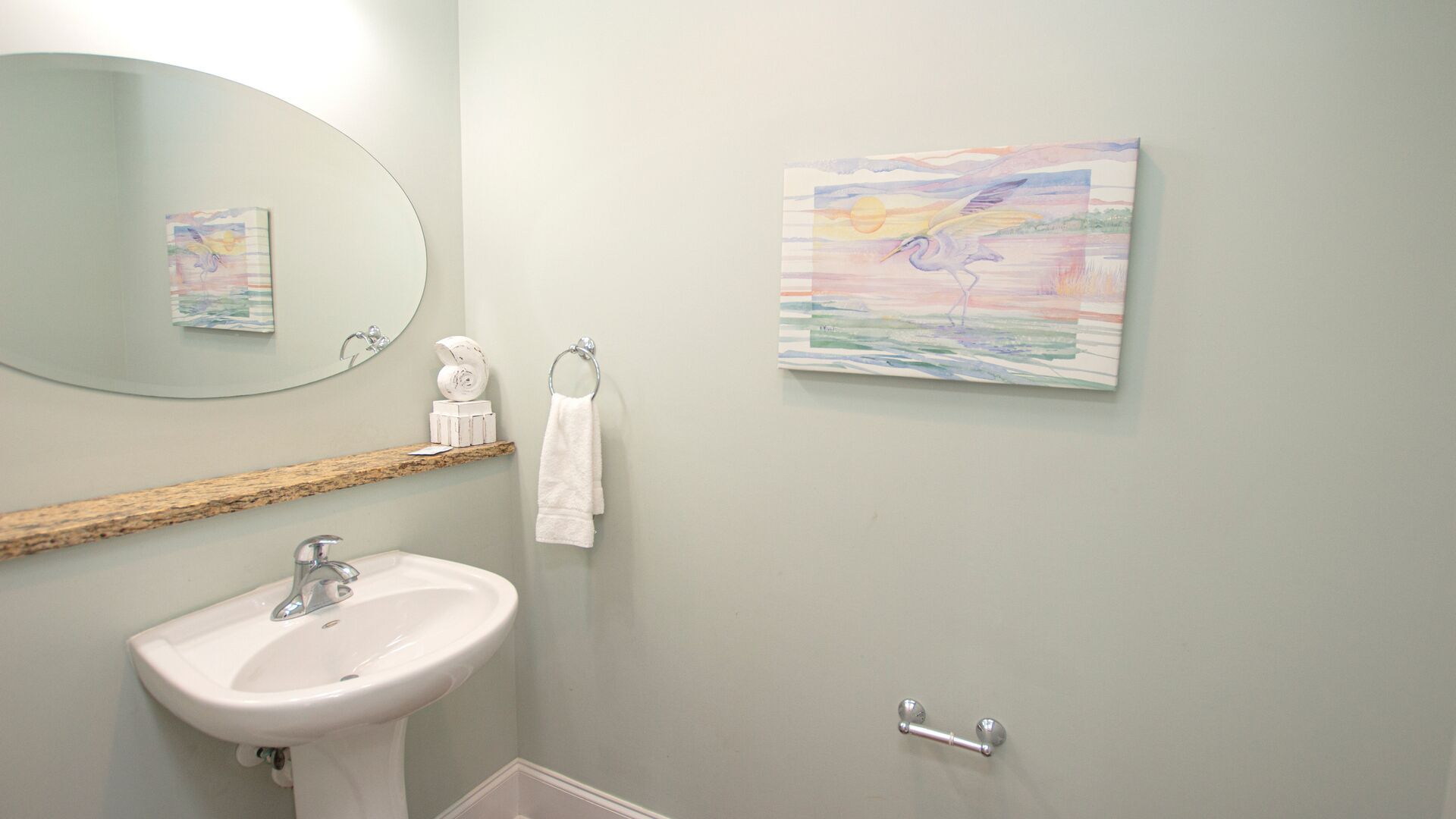 A bathroom with a white sink, a mirror, a towel rack, and two wall-mounted paintings.