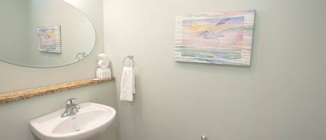 A bathroom with a white sink, a mirror, a towel rack, and two wall-mounted paintings.