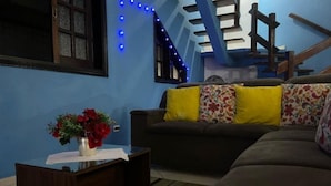 Un salón con un sofá marrón, una mesa de centro con un jarrón de flores rojas y luces de cuerda azules en la pared.