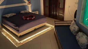Un dormitorio con cama, mesita de noche y una zona de estar con cojines.