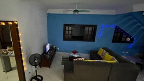 Una sala de estar con un sofá, un televisor, un ventilador y una ventana con luces azules.