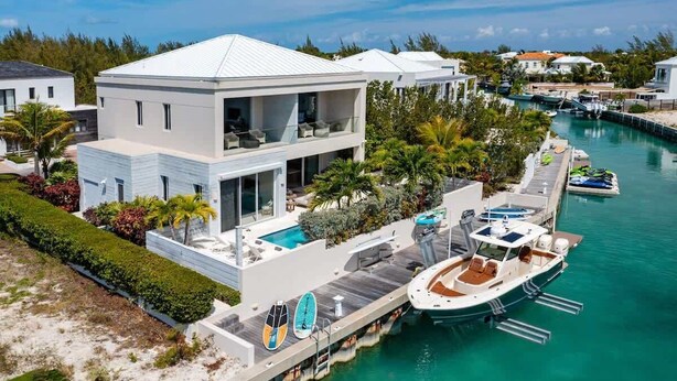 Uma casa moderna de dois andares com piscina, barco atracado e vista para a marina.