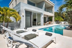A modern two-story house with a swimming pool, outdoor seating, and palm trees. - Canal Front Villa w/ Pool & Balcony Views (Leeward)
