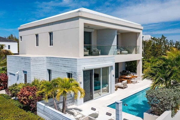 Ein modernes, zweistöckiges Haus mit Pool, Sitzgelegenheiten im Freien und einem Balkon.