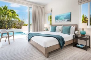 Ein Schlafzimmer mit einem großen Bett, einem Nachttisch, einem Sessel und Blick auf einen Pool und Palmen.
