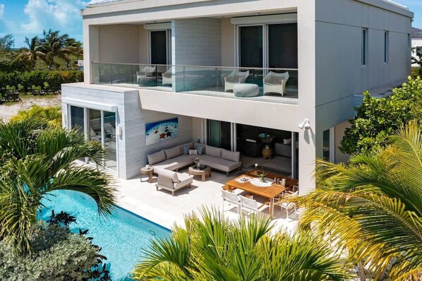 A modern two-story house with a swimming pool, outdoor seating, and lush greenery. - Canal Front Villa w/ Pool & Balcony Views (Leeward)