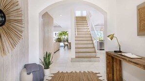 A spacious hallway with a staircase, a wooden bench, a potted plant, and a decorative wall piece. - Salt Air and Second Wind Villas (Leeward)