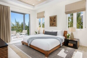 A bedroom with a large bed, a view of the outdoors, and a balcony with seating.