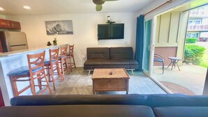 A living area with a sofa, a dining table with chairs, a television, and a ceiling fan. - A Gorgeous Oceanfront Condo! (2BR) (Kapaʻa)