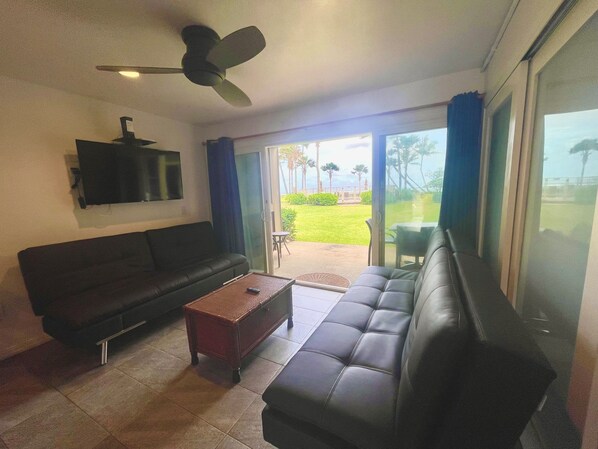 A living room with a sofa, a coffee table, and a television mounted on the wall. - A Gorgeous Oceanfront Condo! 2BR (Kapaʻa)