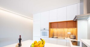 Une cuisine moderne avec des meubles blancs, un mur d’accent en bois, un four encastré et un grille-pain.