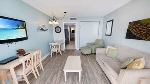 A living room with a TV, a dining table with chairs, a sofa, and a coffee table. - Waterfront condo with balcony & beach access (North Myrtle Beach)