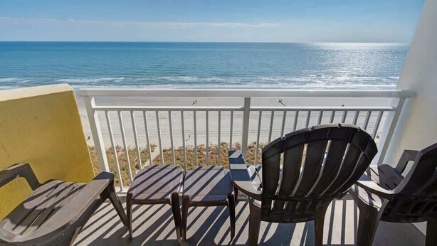 A balcony with a view of the ocean, featuring striped lounge chairs and a yellow wall. - Waterfront condo with balcony & beach access (North Myrtle Beach)