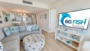 A modern living room with a grey sectional sofa, round ottoman, and a white entertainment unit with decorative items. - Coastal condo with beach access & pools (North Myrtle Beach)