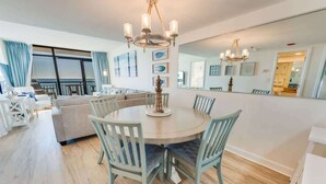 A dining area with a round table and chairs, a chandelier, and a large mirror on the wall. - Coastal condo with beach access & pools (North Myrtle Beach)