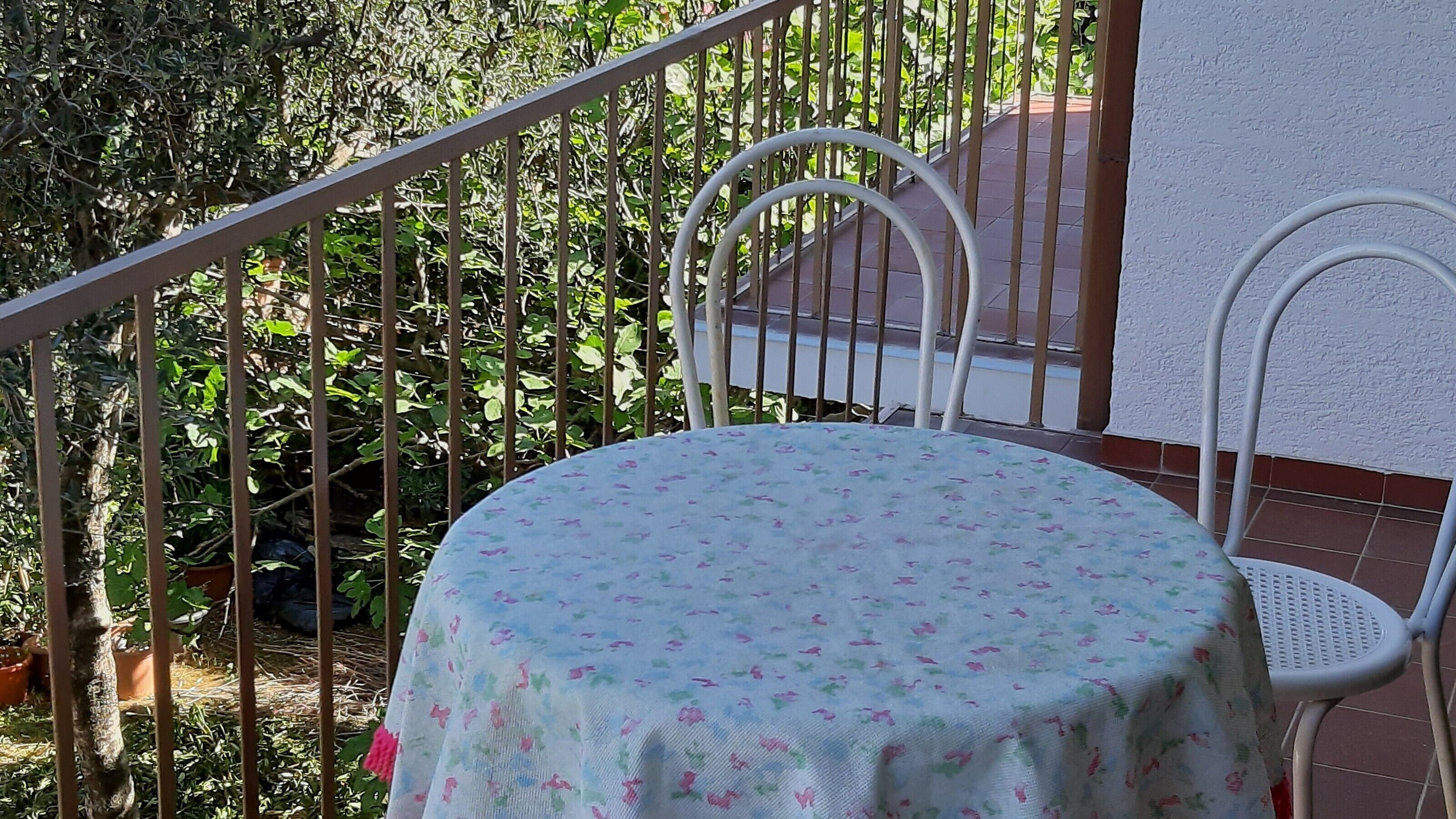 A round table with a floral tablecloth, a white chair, and a metal railing.