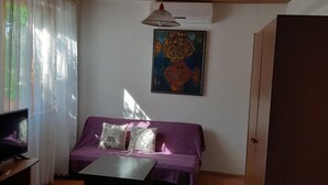 Una sala de estar con un sofá púrpura, un televisor de pantalla plana, un cuadro de un pez y un equipo de aire acondicionado.