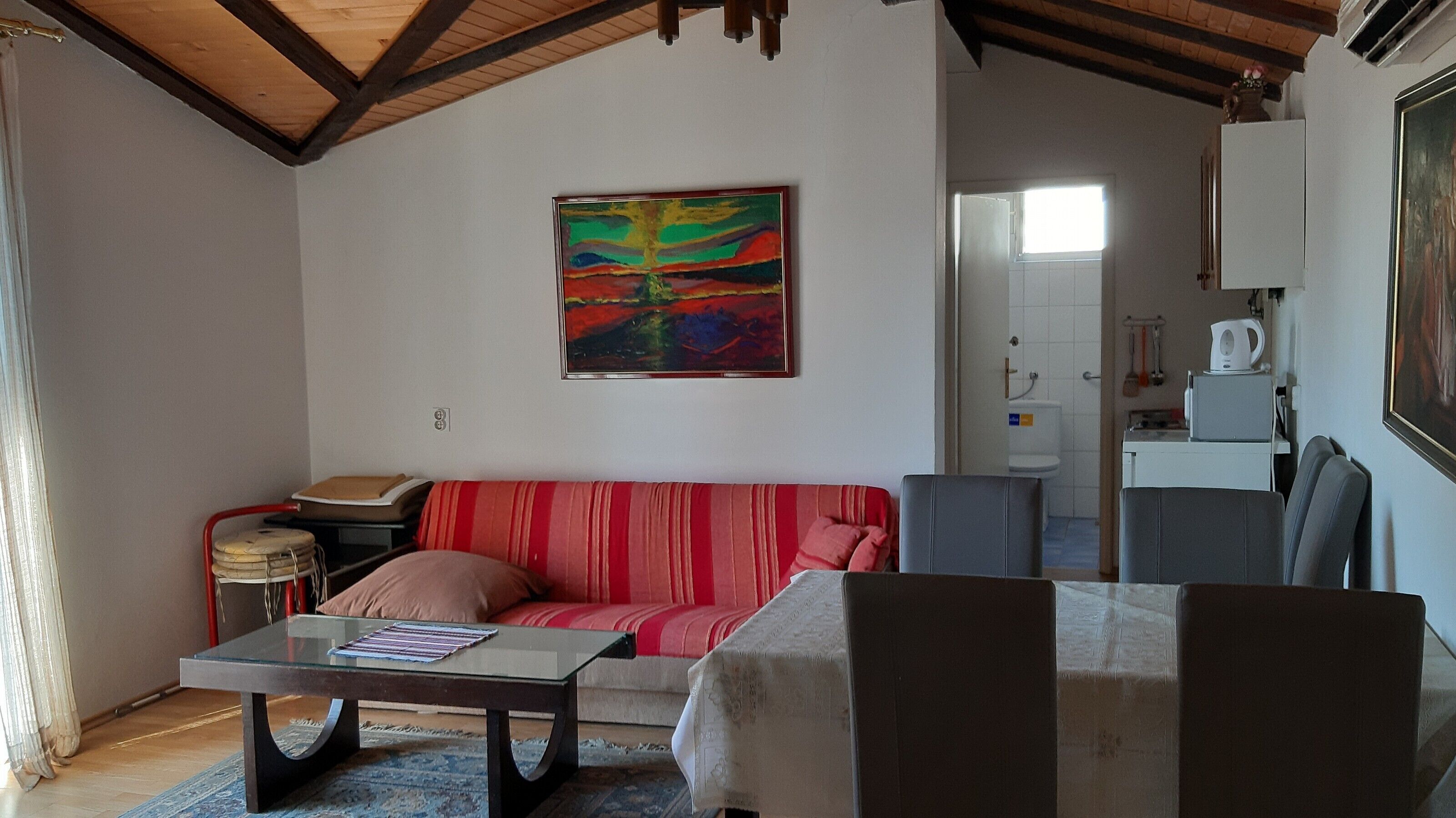 A living room with a red-striped sofa, a glass coffee table, and a painting on the wall.