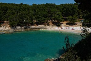 A beach with clear turquoise water, surrounded by dense green trees and rocky cliffs. - Apartment Point - Two Bedroom Apartment with Balcony (Pula)