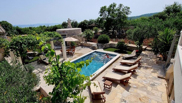 Une piscine entourée de carreaux de pierre, avec des chaises longues et une pergola.