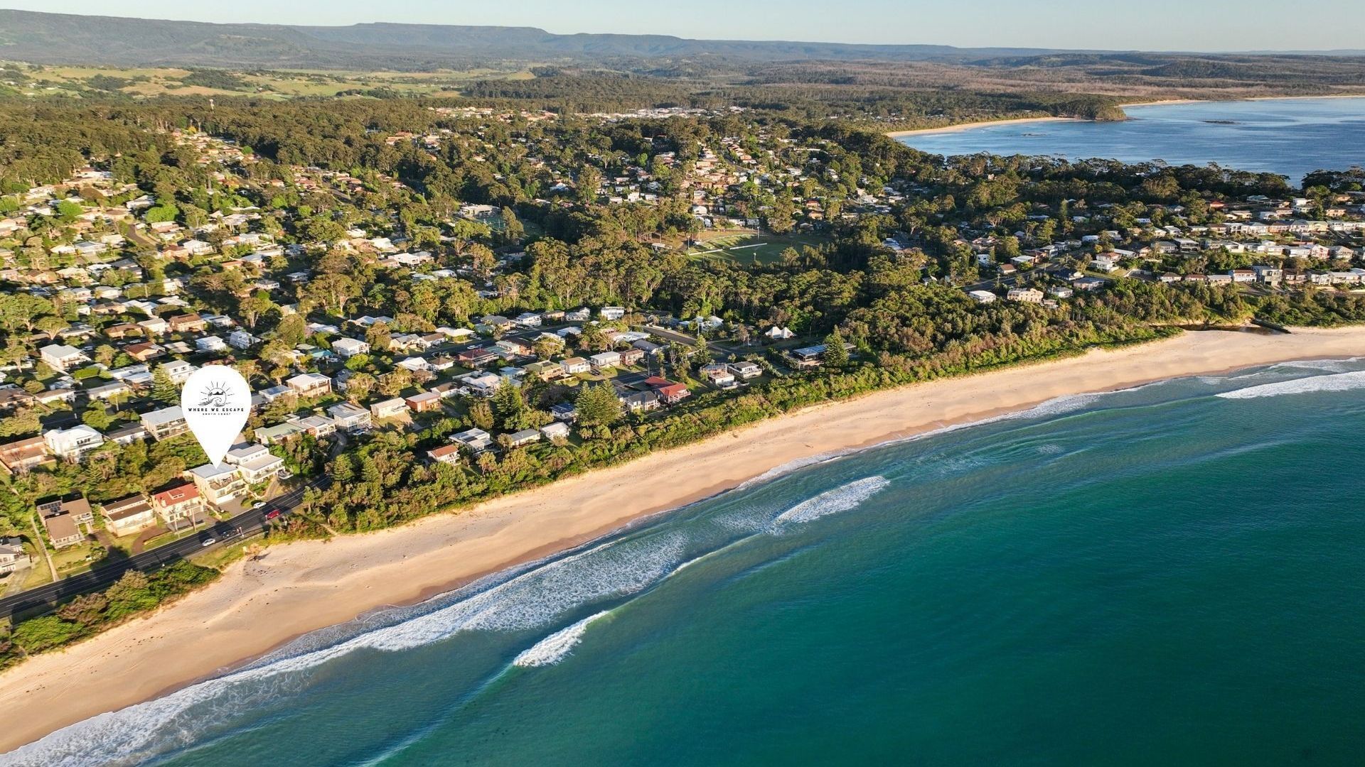 An aerial view of a coastal residential area with houses, a beach, and a large body of water.